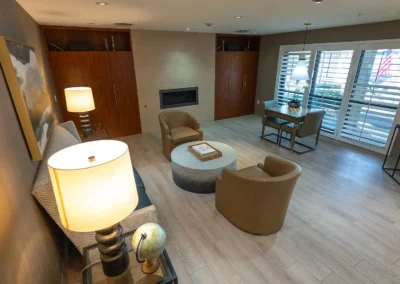 Cozy lounge with warm lighting, fireplace, two armchairs, coffee table, and chess table near large windows.