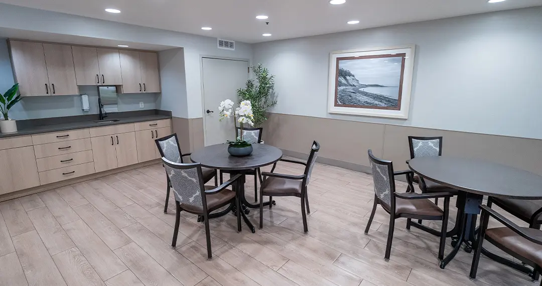 Home - Amenities4 A small conference or meeting room with a long oval table surrounded by gray chairs and framed artwork on the wall.